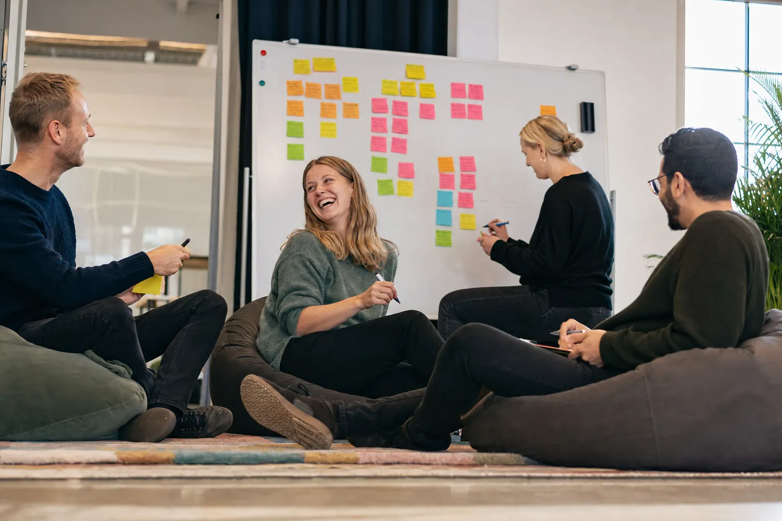A relaxed team sitting together in a check-in, reviewing sticky notes on a whiteboard