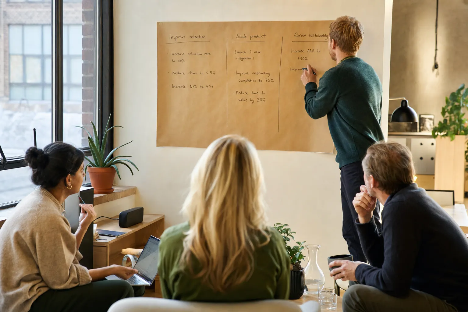 A small team in a bright Nordic office, one person writing measurable results under theme headings on a paper sheet while colleagues contribute